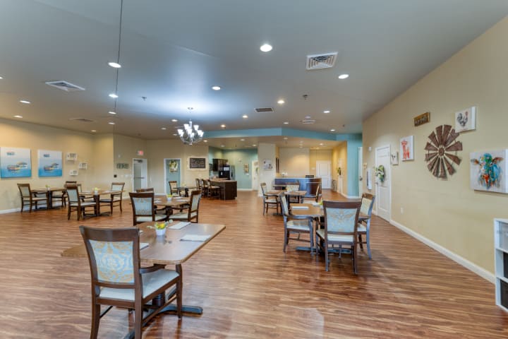 A spacious and well-lit dining area with tables and chairs arranged neatly on a wooden floor.