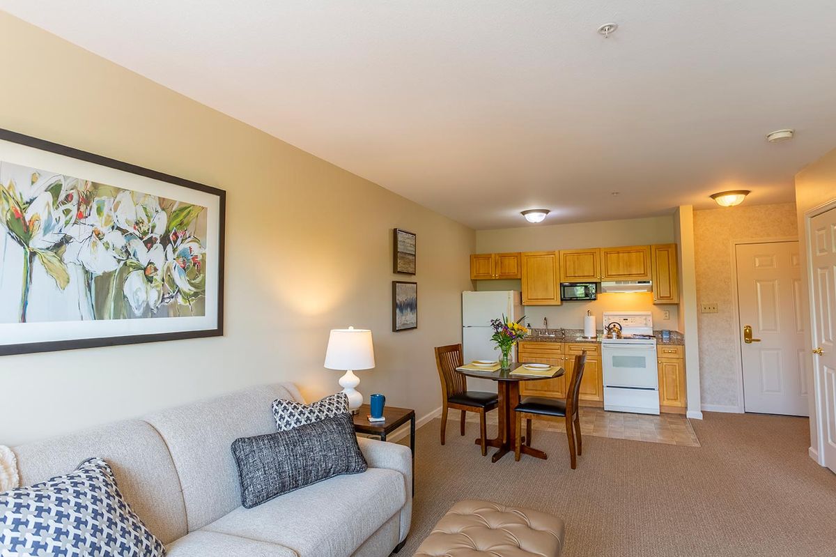 A cozy apartment interior featuring a living room with a sofa and lamp, and an adjoining kitchen and dining area.