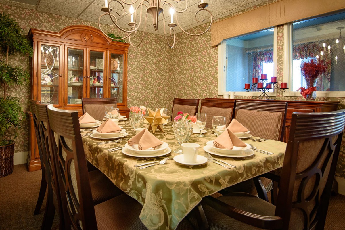 An elegantly set dining room table with a chandelier overhead and a china cabinet in the corner.