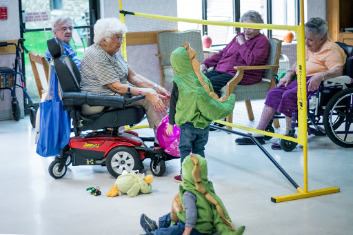 Children in playful costumes engage with elderly residents in a community setting.