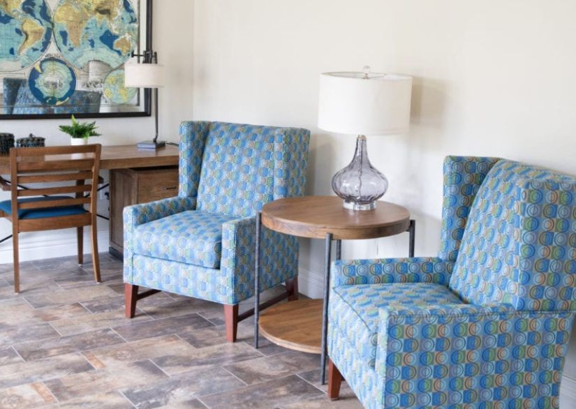 A cozy living room setup with patterned blue armchairs, a wooden side table, and a stylish lamp.