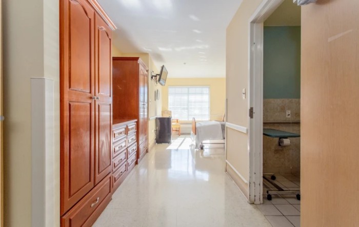 A hospital patient room with wooden cabinets, a bed, and a bright window.