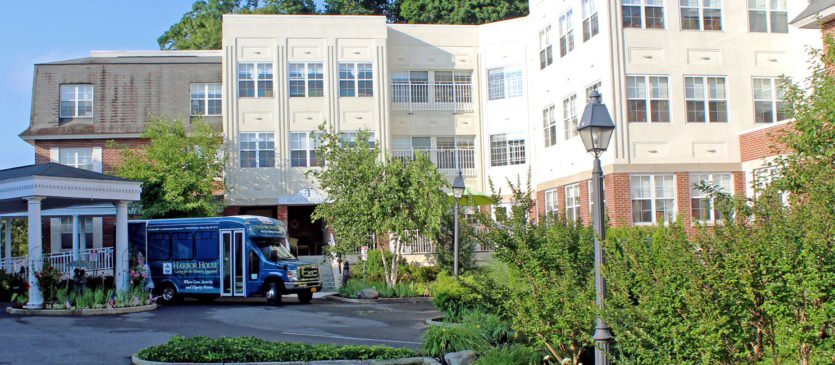 A view of a building with a bus parked nearby, surrounded by greenery.