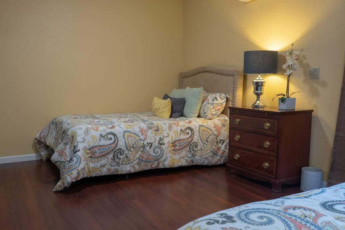A cozy bedroom with a single bed adorned with patterned bedding, a lamp on a nightstand, and decorative pillows.