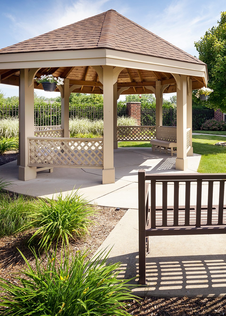 A serene park scene featuring a wooden gazebo surrounded by benches and lush greenery.