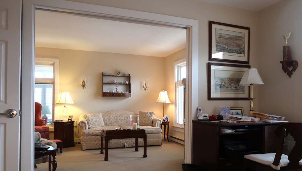 A cozy living room with classical decor, featuring a comfortable sofa, warm lighting from lamps, and framed art on the walls.
