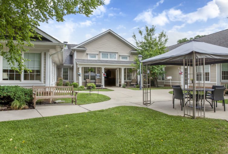 A well-maintained garden area with benches and a canopy in front of a residential building.