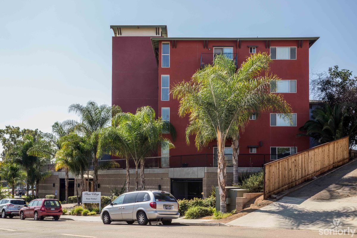 A modern hotel building surrounded by palm trees with a car parked on the street.