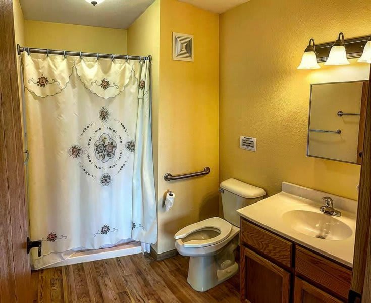 A bathroom with yellow walls, featuring a toilet, sink, and shower with a decorative curtain.