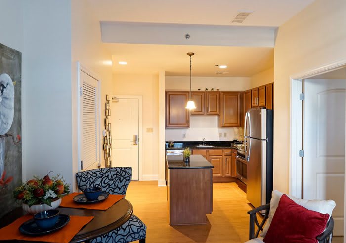 A modern apartment kitchen with an adjacent dining area, featuring wooden cabinets and stainless steel appliances.
