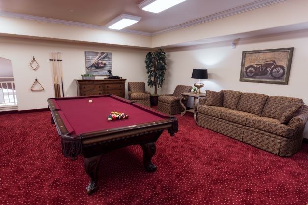 A cozy billiard room featuring a pool table with red felt, surrounded by comfortable seating and warm lighting.