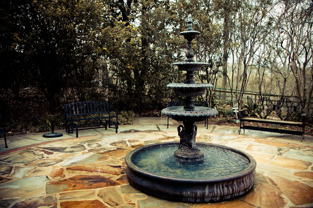 A multi-tiered fountain in a serene garden setting, surrounded by nature.