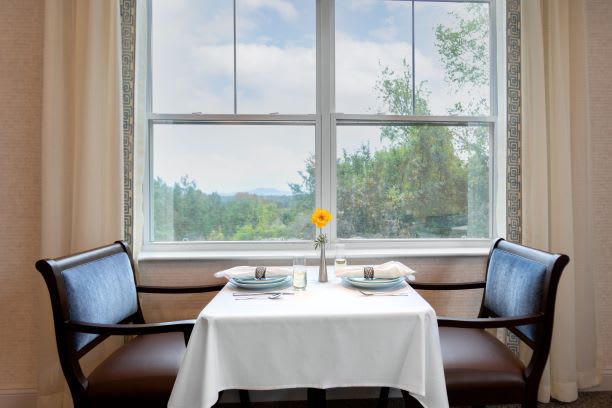 A cozy dining setup for two with a sunflower centerpiece, offering a scenic window view.
