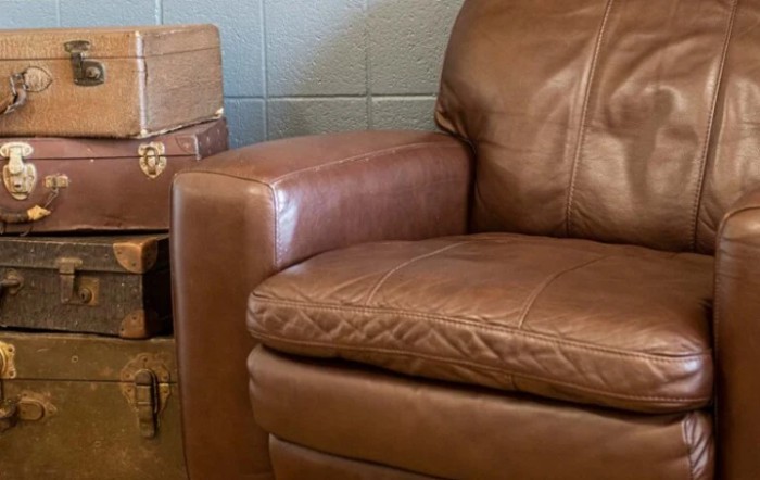 A comfortable brown leather sofa with a cozy armrest, accompanied by stacked vintage suitcases in a living room setting.