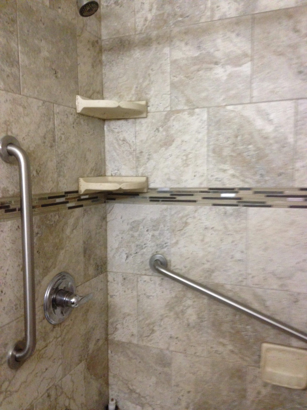 A bathroom shower with tiled walls, equipped with grab bars and soap holders.