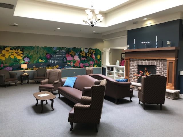 A cozy lounge area with sofas, armchairs, and a fireplace, featuring a colorful mural on the wall.