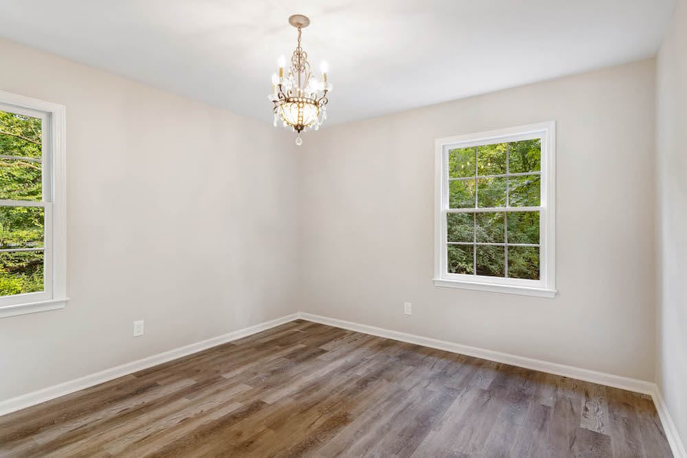 A bright, empty room with hardwood floors and a chandelier.