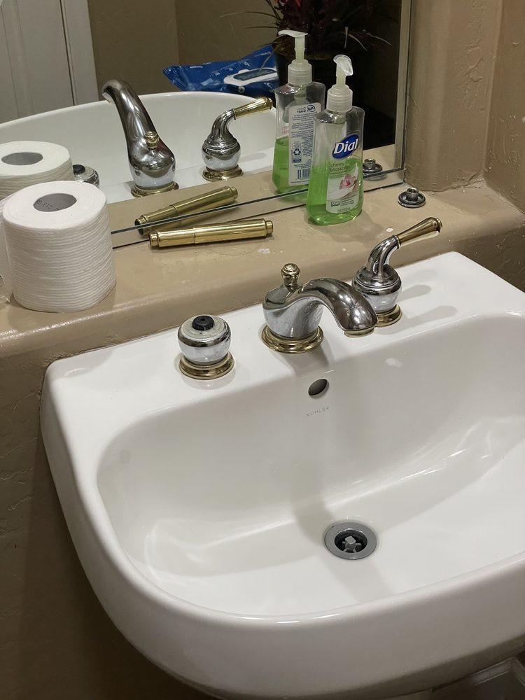 A bathroom sink with a faucet, mirror, soap dispenser, and toilet paper rolls.