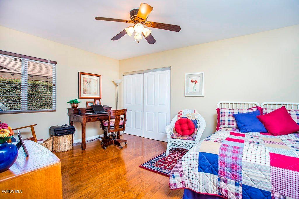 A cozy bedroom featuring a bed with a colorful quilt, a wooden desk, and a ceiling fan.