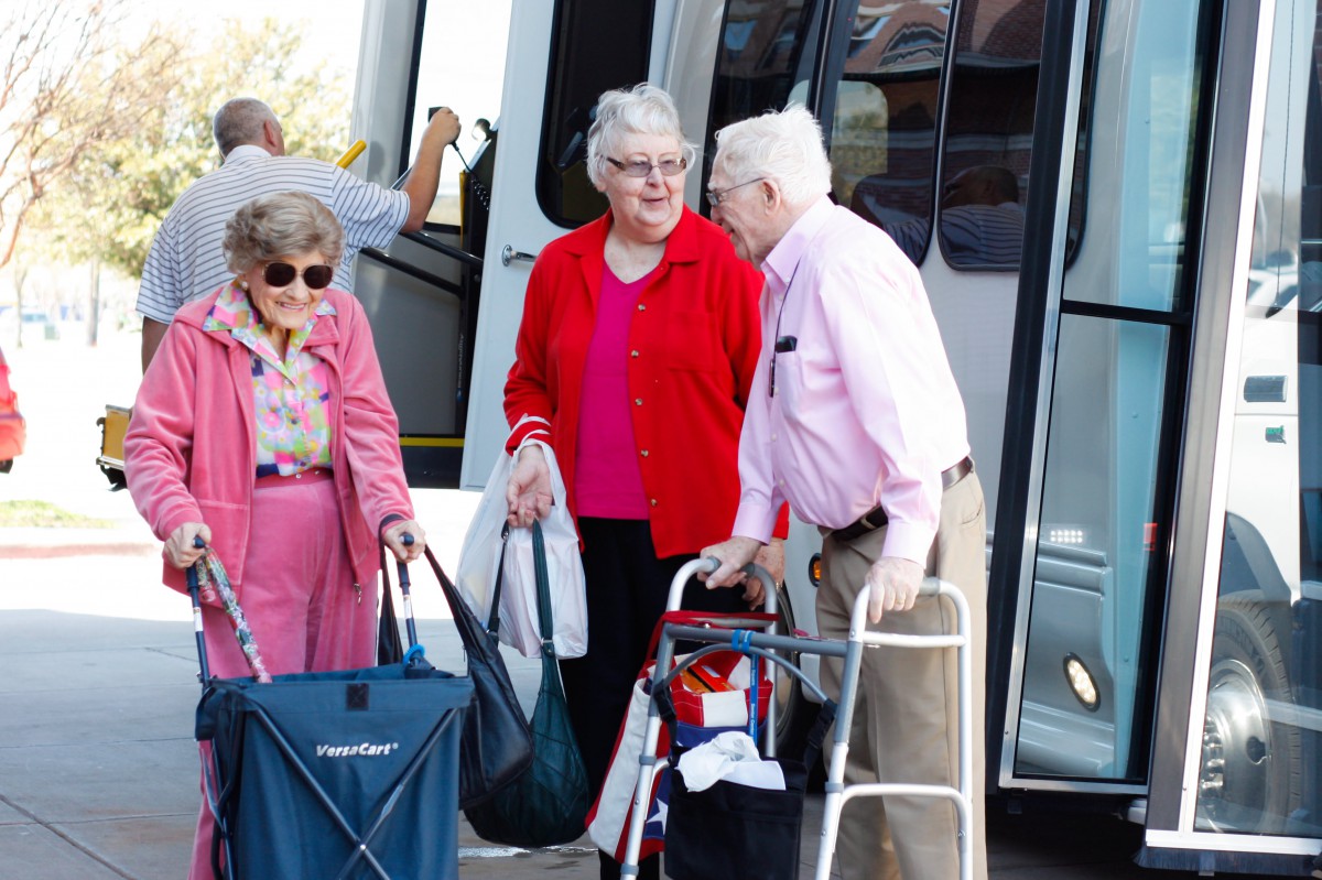 A group of elderly people with luggage and walking aids getting off a bus.