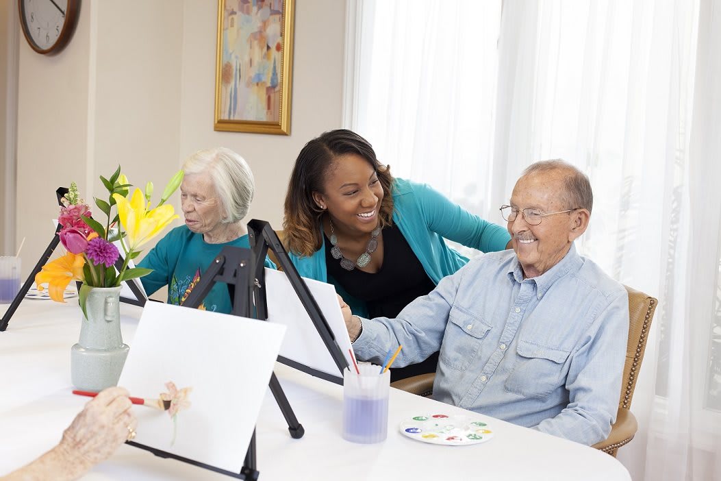 A caregiver assisting elderly individuals in a painting class.