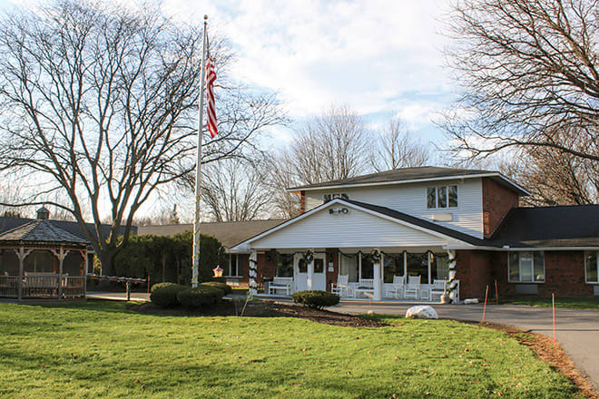 A two-story house with a front porch and an American flag flying in the yard.