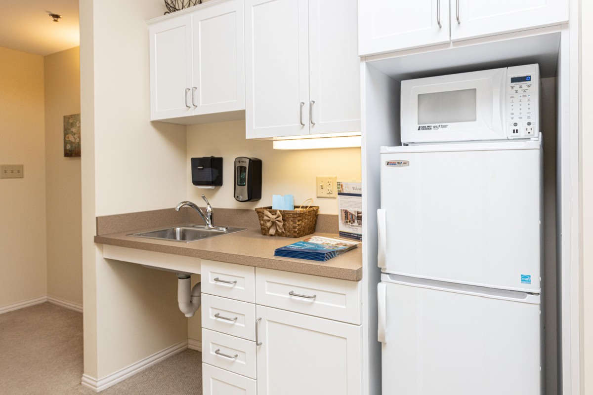 A compact kitchenette with a sink, white cabinets, and essential appliances like a refrigerator and microwave.