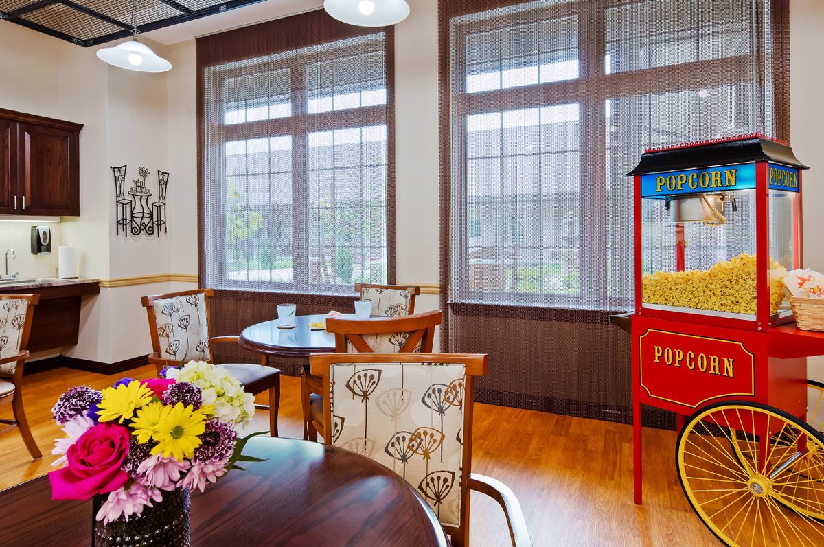 A cozy cafe interior featuring tables and chairs, a popcorn machine, and a vase of flowers by large windows.