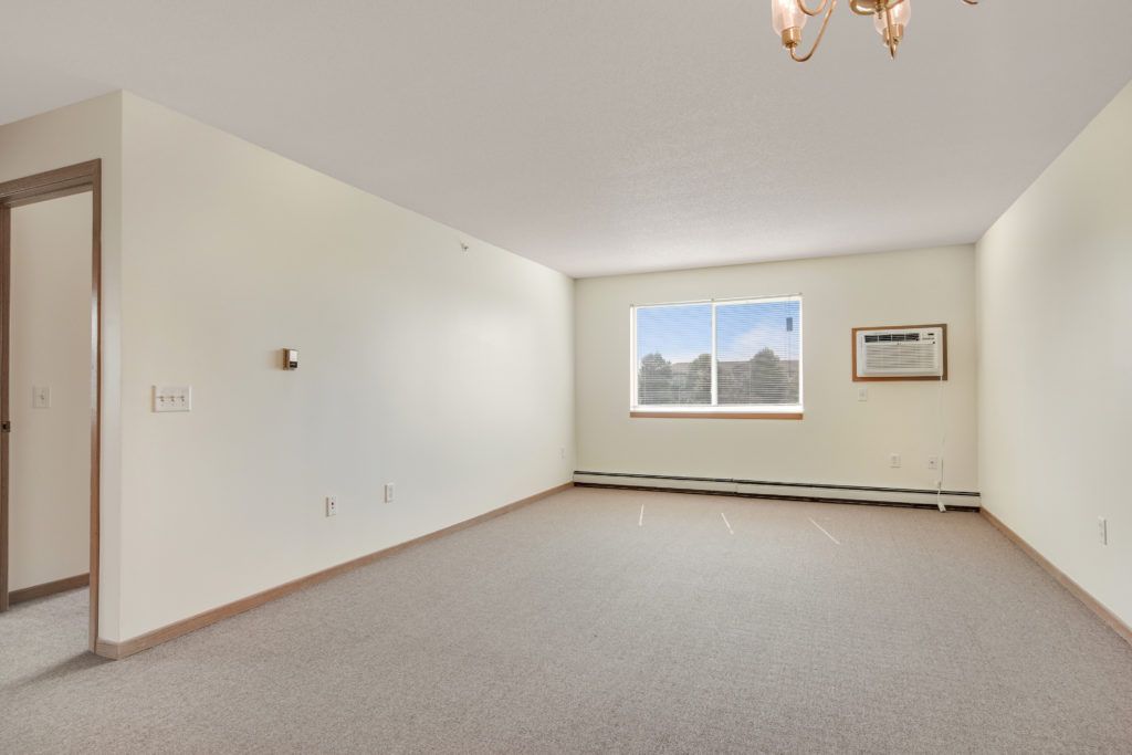 An empty living room with a window, air conditioner, and chandelier.