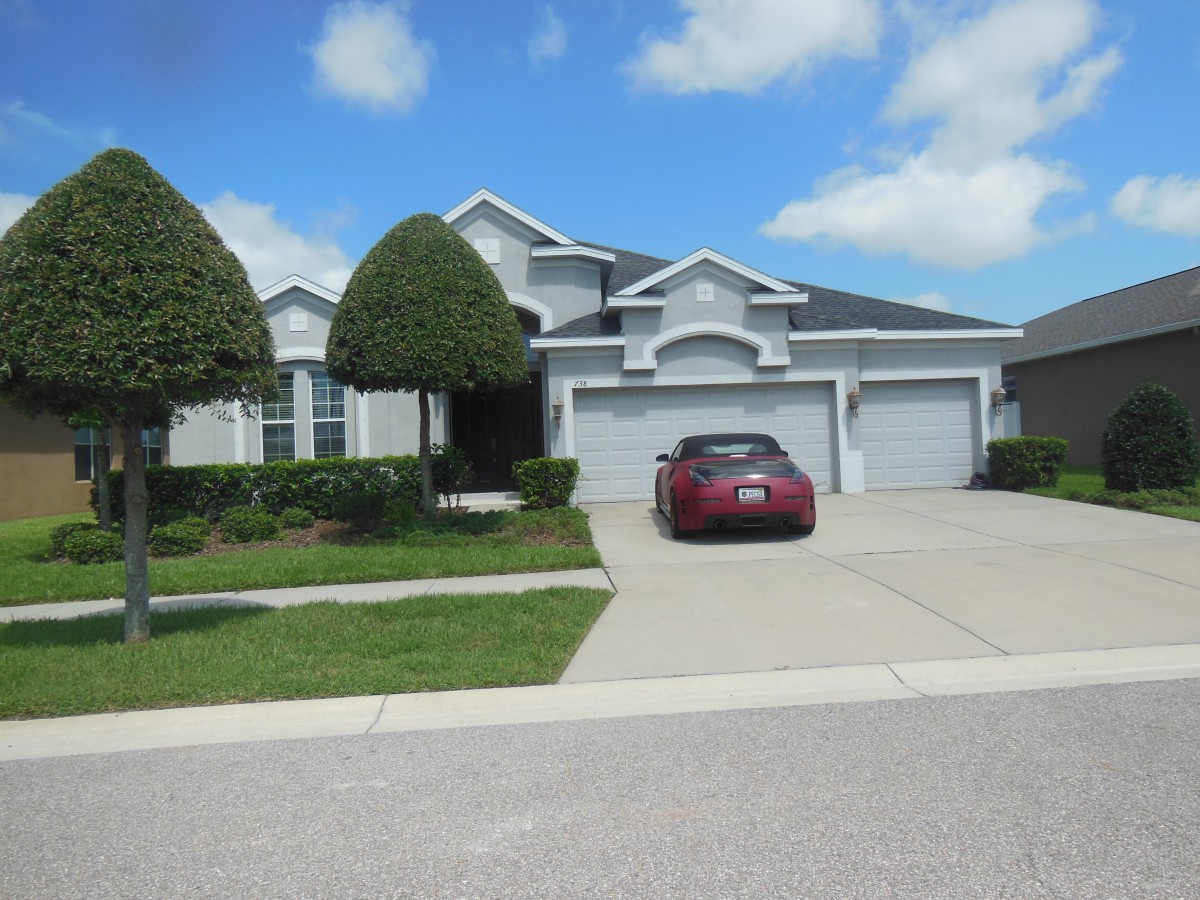 A suburban house with a neatly trimmed lawn and a car parked in the driveway under a cloudy sky.