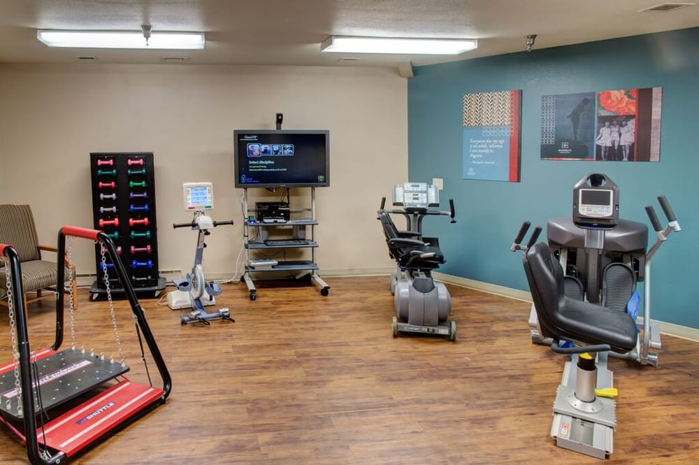 A fitness room equipped with various exercise machines including treadmills and stationary bikes, featuring a wooden floor and a television on the wall.