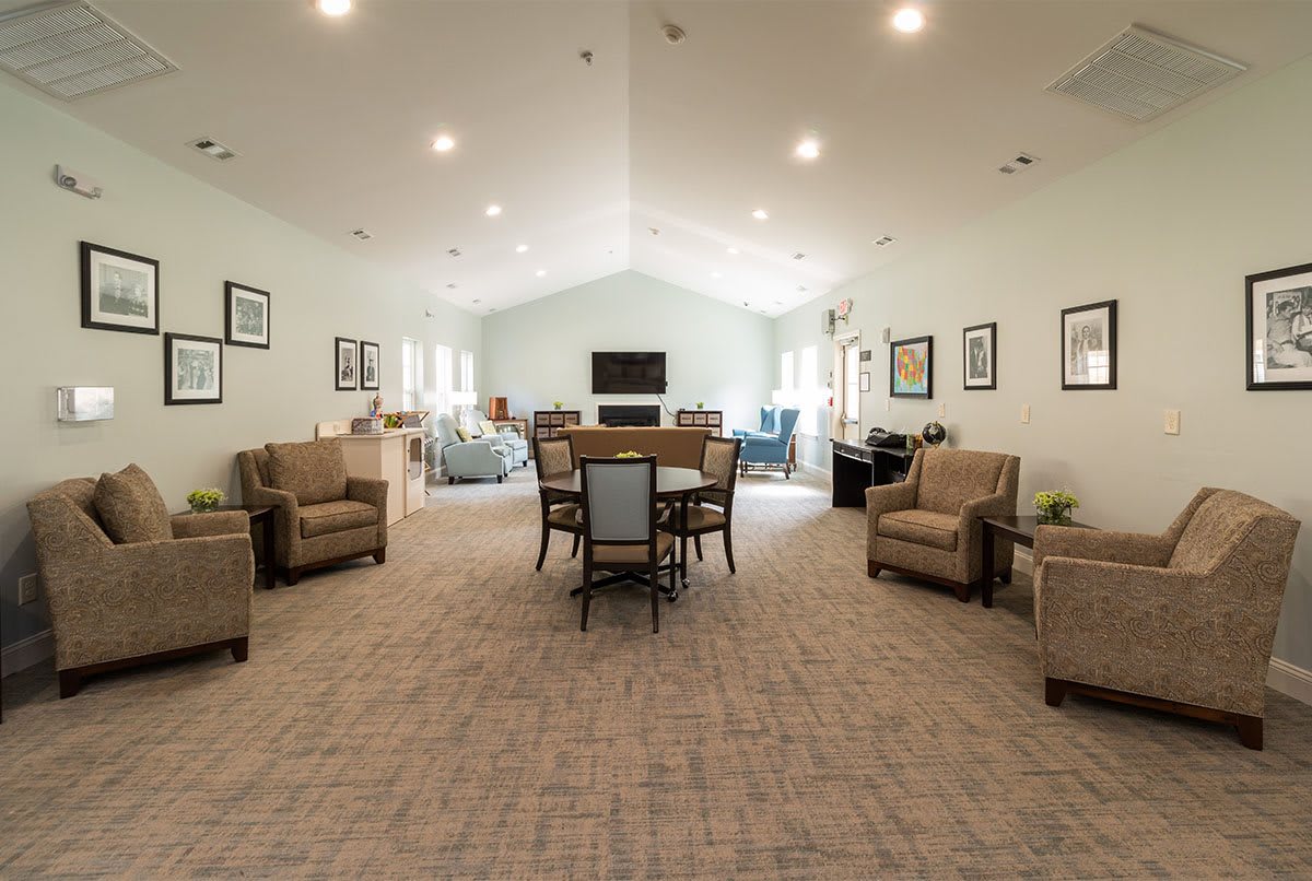 A spacious living room with arranged sofas and a central table surrounded by chairs, well-lit with ceiling lights.