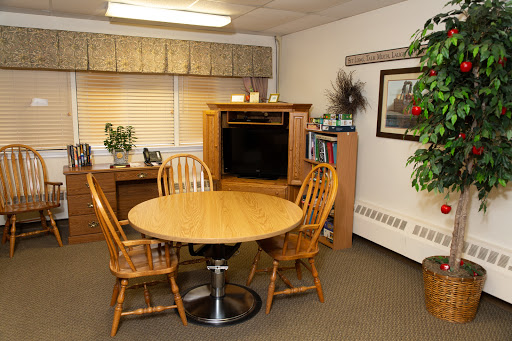 A cozy dining area featuring a round wooden table and four chairs, complemented by a TV stand and decorative plants.