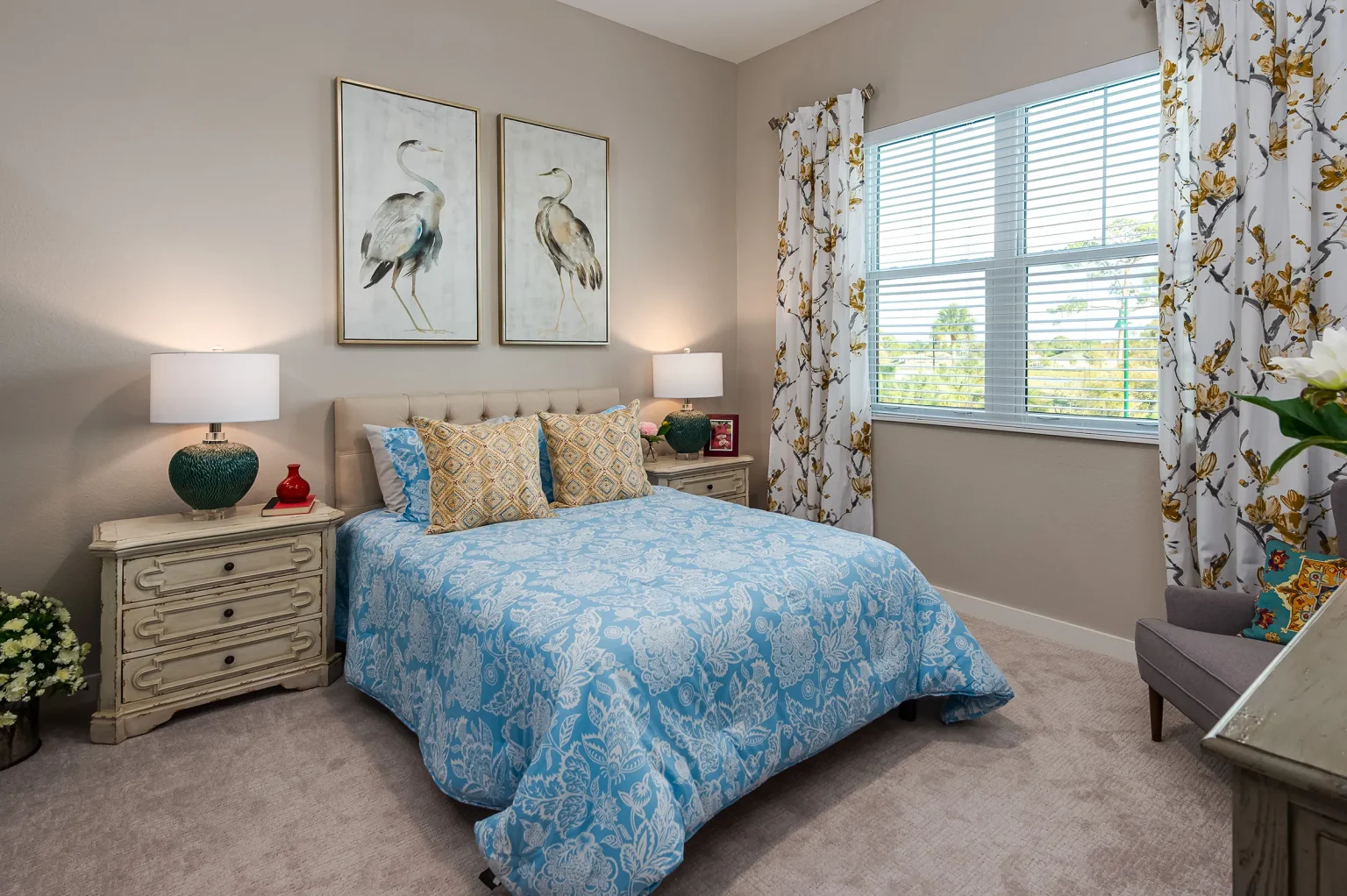 A cozy and well-decorated bedroom featuring a bed with blue bedding, framed artwork above the headboard, and nightstands with lamps on each side.