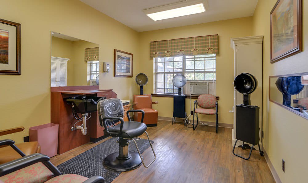 A cozy hair salon interior featuring salon chairs, dryer stations, and a large window with natural light.
