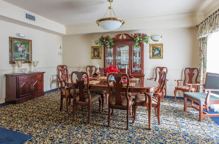 A traditional dining room with a wooden table and chairs, ornate carpet, and chandelier.