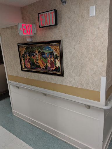A hospital corridor featuring a decorative artwork on the wall and an exit sign above.