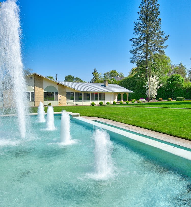 A beautiful house with a large fountain and well-manicured lawn under a clear blue sky.