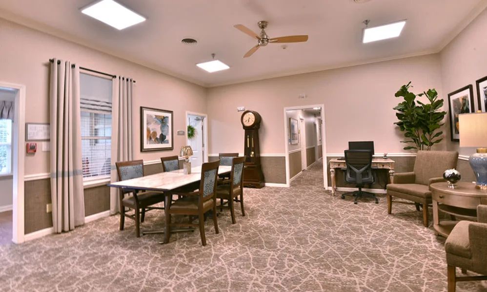 A well-lit conference room with a large table and chairs, featuring a grandfather clock and carpeted floors.