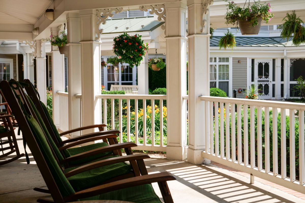 A sunny porch with rocking chairs overlooking a garden and house.