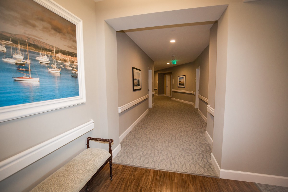A well-lit corridor with framed artwork, featuring a bench and carpeted flooring.