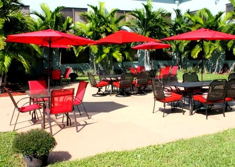 Outdoor patio area with red umbrellas and seating amidst tropical plants.