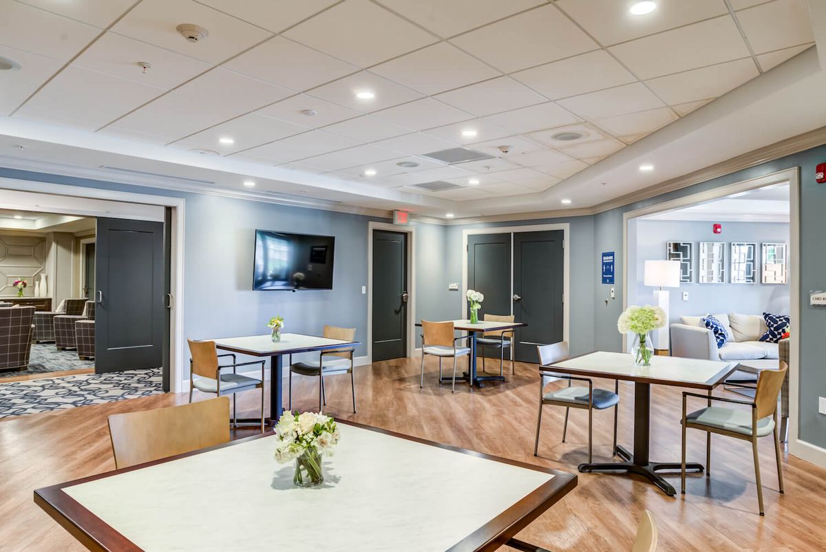 A modern dining area with several tables, chairs, and a television, featuring wooden floors and floral decorations.