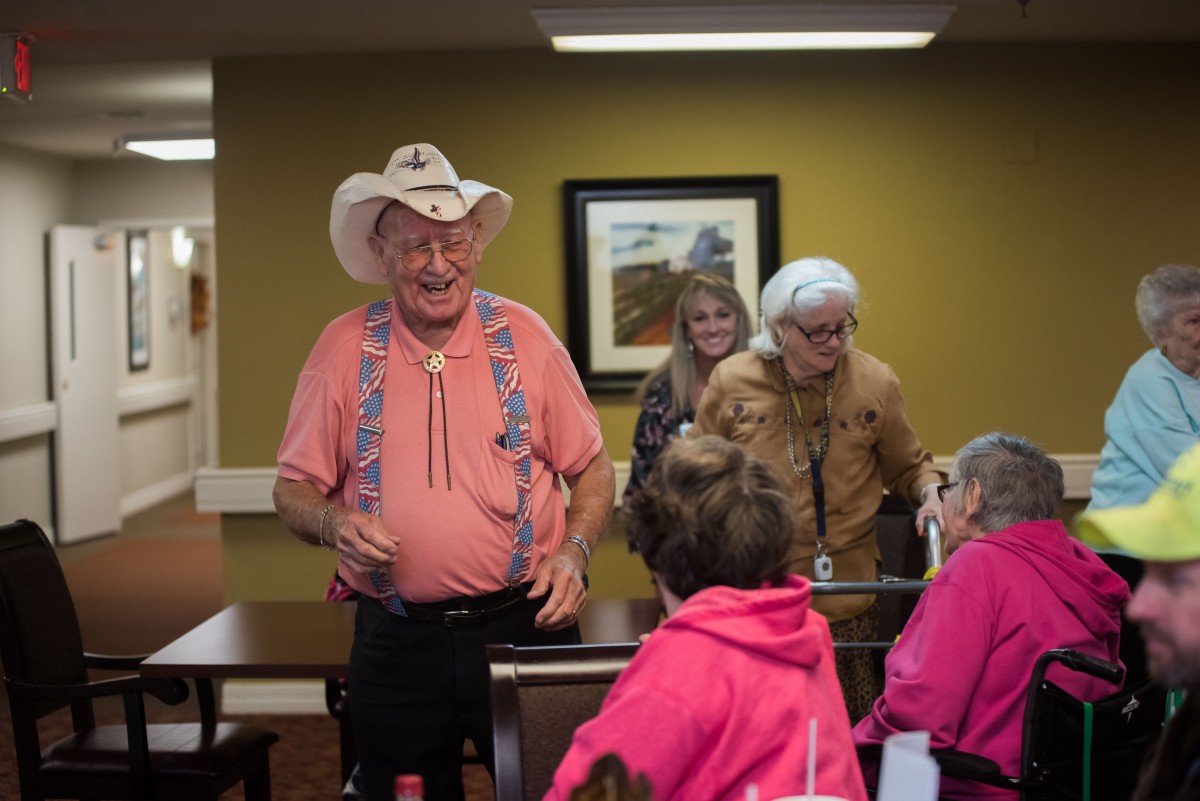 A cheerful group of elderly people interacting indoors, with one wearing a cowboy hat.