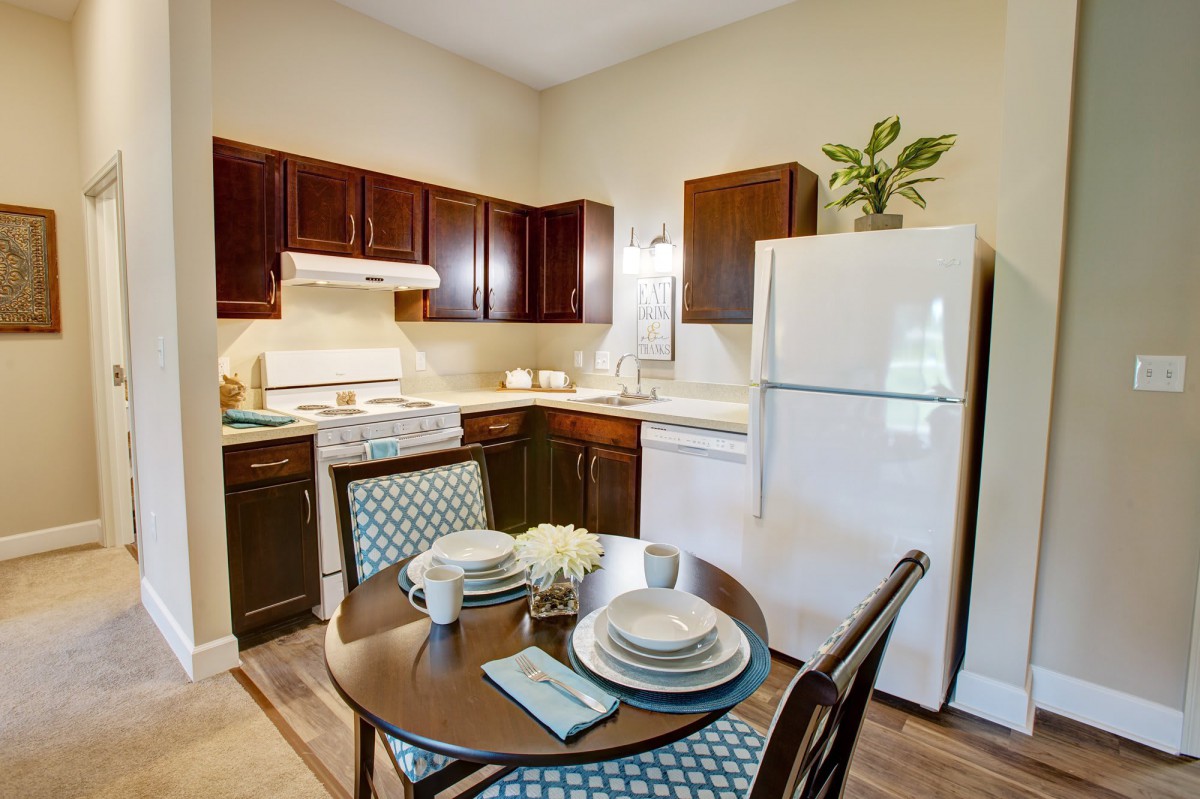 A cozy kitchen with dark wood cabinets, a white refrigerator, and a round dining table set for two.