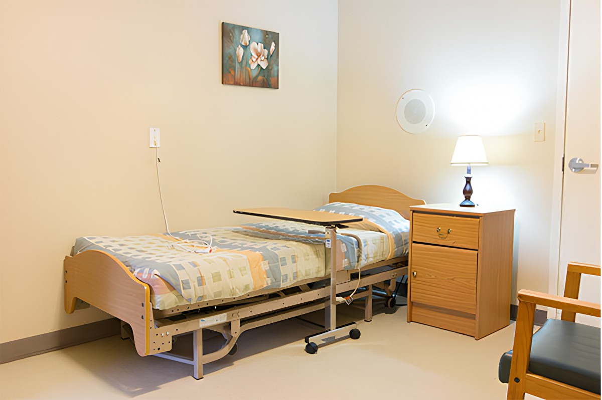 A simple room with a hospital bed, nightstand, and lamp.