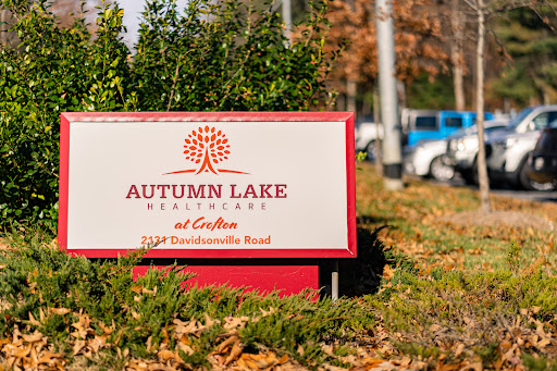A welcoming sign for Autumn Lake, surrounded by greenery and an autumn backdrop.