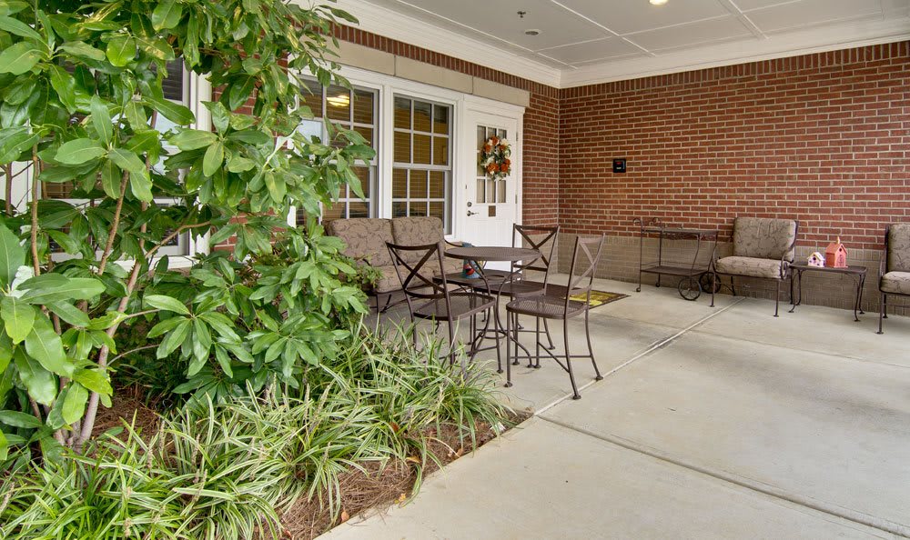 A cozy outdoor patio setup with chairs and a table next to lush greenery and a brick wall.