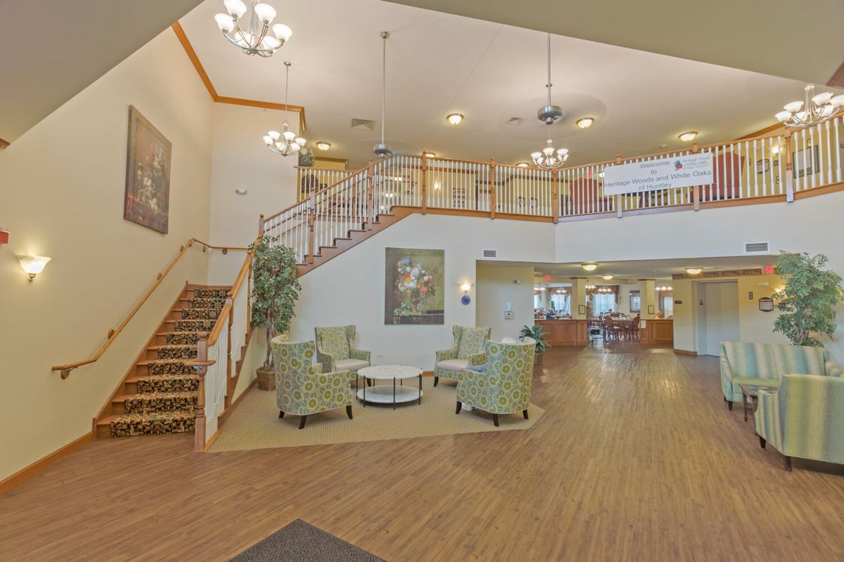 A spacious and elegantly designed lobby area with a staircase, seating arrangement, and chandeliers.