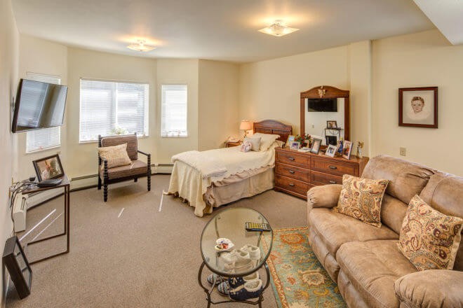 A cozy bedroom with a bed, dresser, sofa, and large windows.